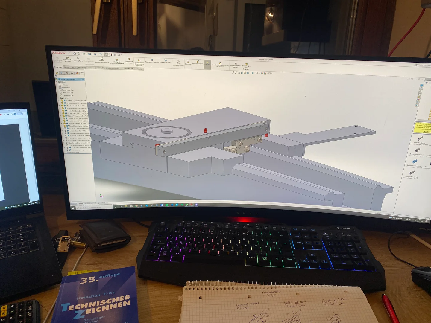 CAD-Arbeitsplatz mit Baugruppenmodell, Handskizze und Fachbuch.